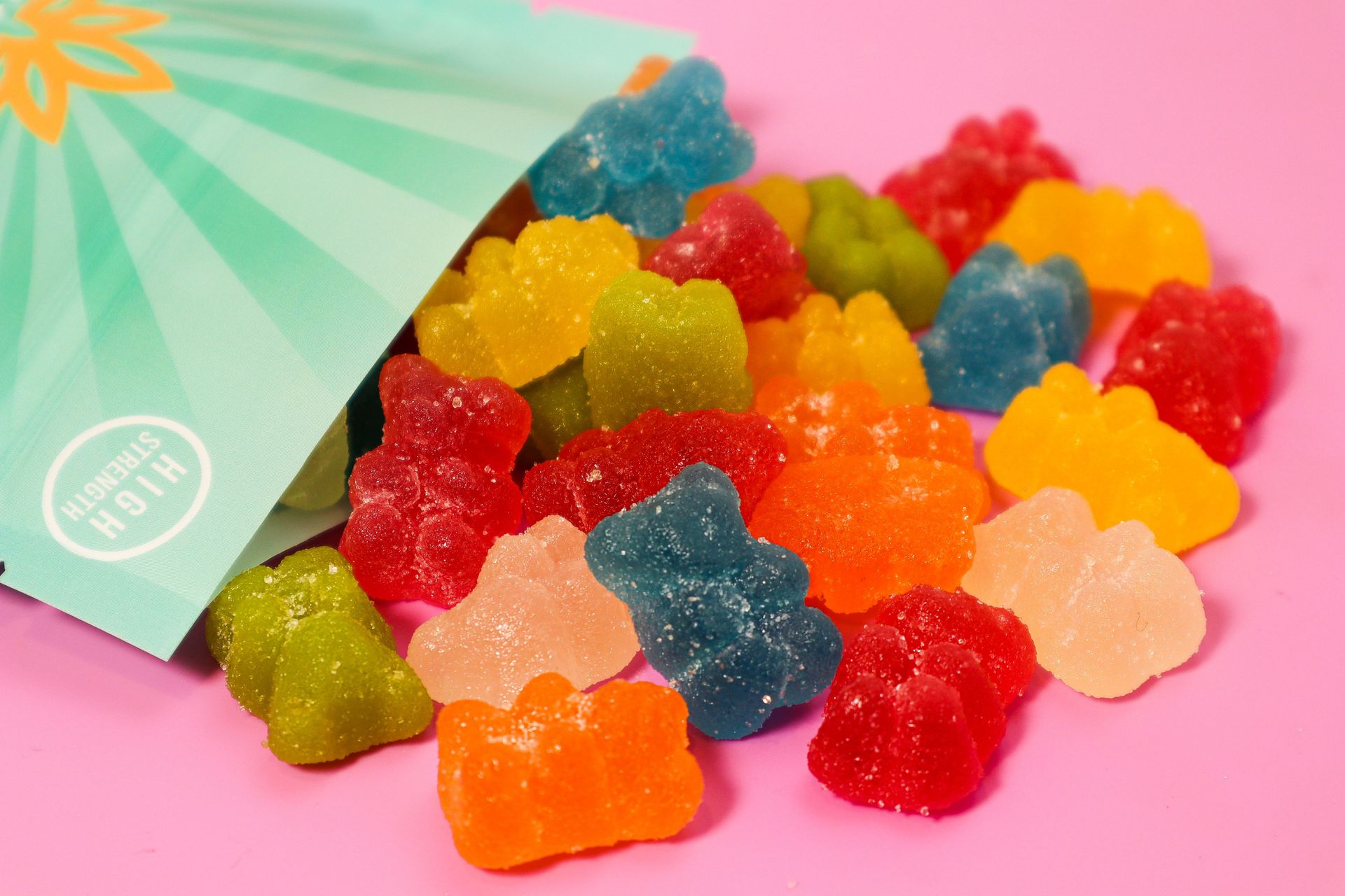 Close-up of colorful gummy bears spilling out of a high-strength package on a pink surface.